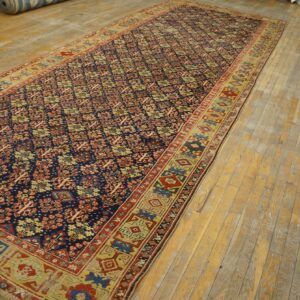 A long traditional runner rug with a navy, red, and gold repeating pattern lies on worn wood floors.