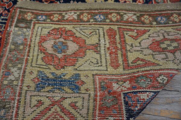 A detailed view of a traditional rug border in red, gold, and blue resting on weathered wood.