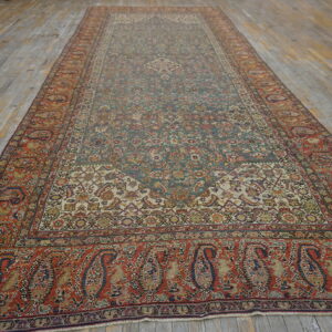 Long traditional rug with a detailed muted green and cream field and wide red paisley borders on wood planks.