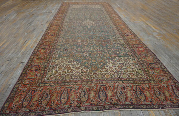 Long traditional rug with a detailed muted green and cream field and wide red paisley borders on wood planks.