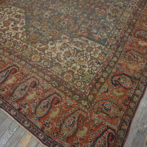 Intricate low-pile rug showing teal, rust, and ivory patterns rests on distressed gray wooden planks.