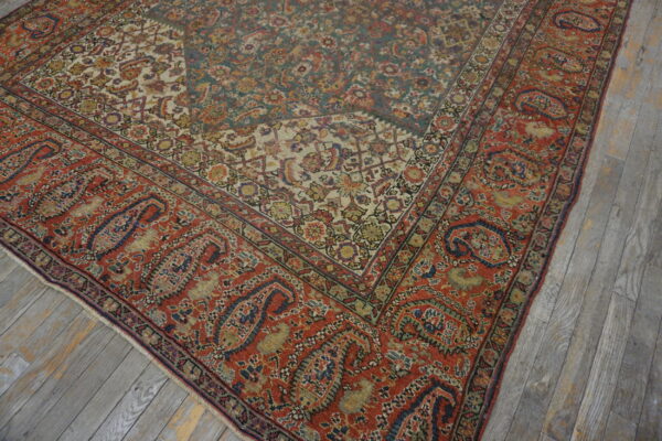 Intricate low-pile rug showing teal, rust, and ivory patterns rests on distressed gray wooden planks.