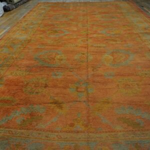 Large low-pile orange rug featuring sage green and gold traditional patterns on wood flooring.