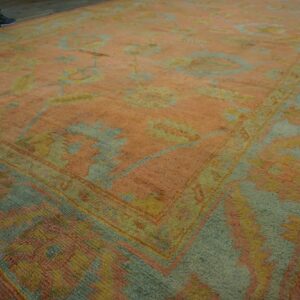 Low-angle view of a large rug in faded peach, pale blue, and yellow floral patterns on wood flooring.