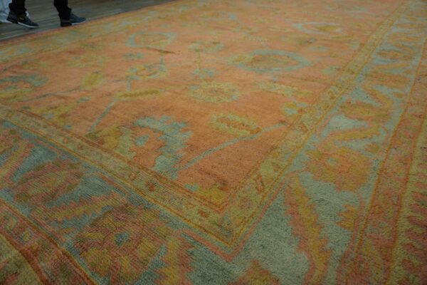 Low-angle view of a large rug in faded peach, pale blue, and yellow floral patterns on wood flooring.