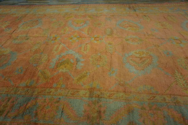 Peach-toned low-pile rug with a traditional floral pattern in sage green and pale yellow on wood floors.