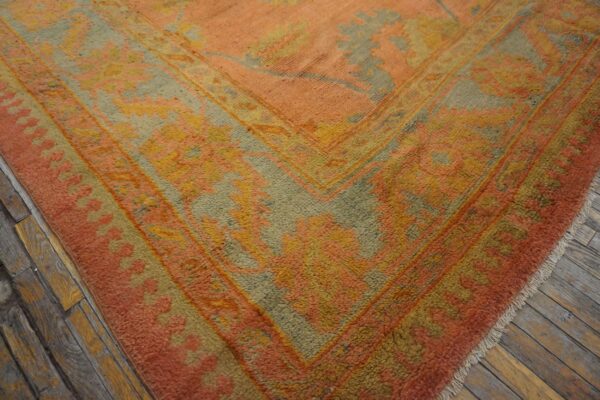 Textured orange, gold, and sage geometric rug corner resting on rustic wood plank flooring.