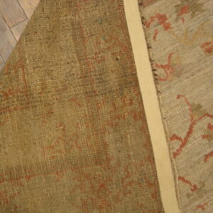 Beige and terracotta patterned rug is folded back revealing its olive woven reverse on wood flooring.