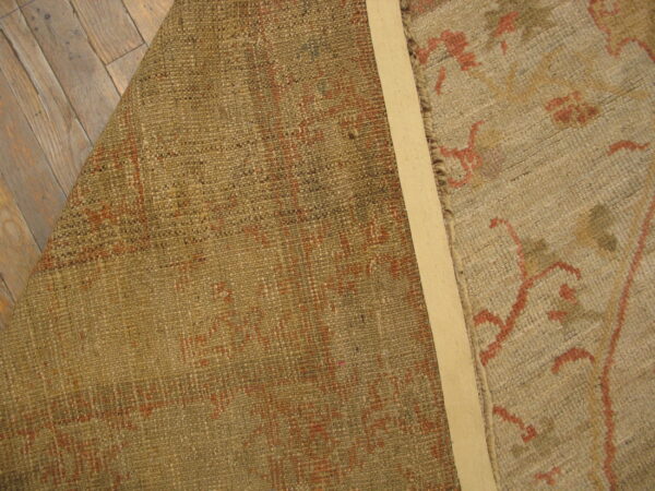 Beige and terracotta patterned rug is folded back revealing its olive woven reverse on wood flooring.