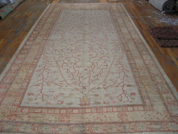 Light beige rug with a sparse red vine pattern and geometric borders covers a wood floor.