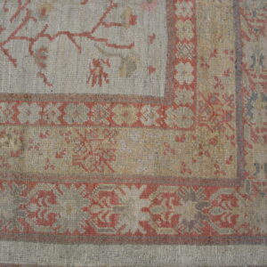 Low-pile rug corner in gray and tan with rust botanical patterns visible over hardwood planks.