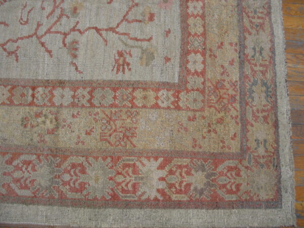 Low-pile rug corner in gray and tan with rust botanical patterns visible over hardwood planks.