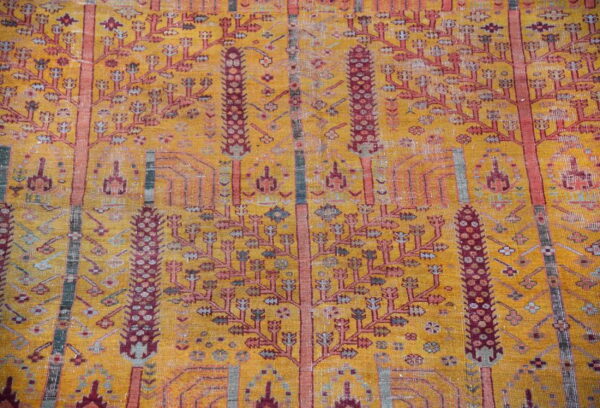 Ocher field rug with distressed texture and vertical columns of maroon and pink stylized trees.