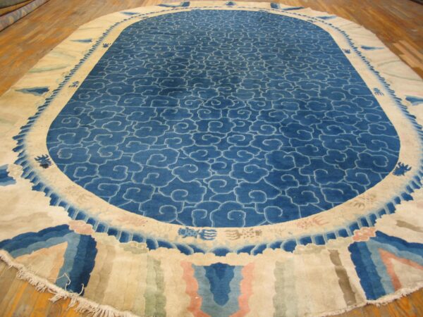Large oval rug with a blue cloud motif field and a wide cream, pink, and blue decorative border.