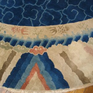 Close-up of a round rug showing blue cloud motifs and a colorful border of stylized waves and mountains.
