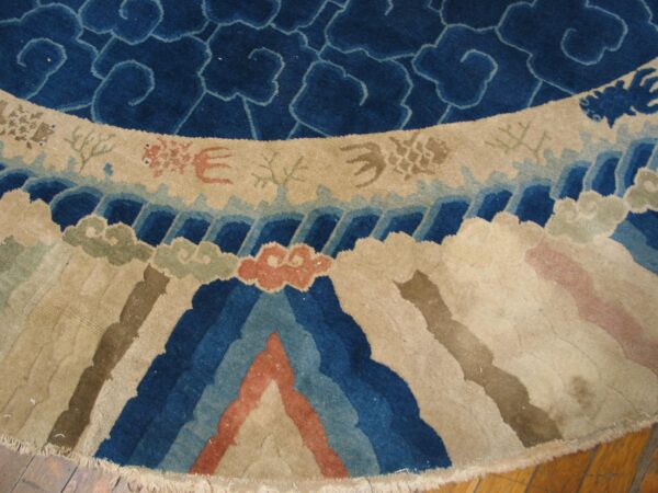 Close-up of a round rug showing blue cloud motifs and a colorful border of stylized waves and mountains.