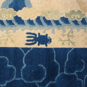Plush rug detail featuring blue waves, beige clouds, a stylized creature, and dense indigo scrollwork.