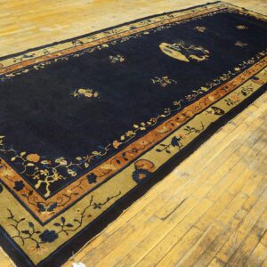 Long navy blue rug with gold and rust floral borders and central pictorial motif on worn wood flooring.