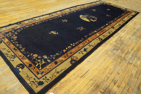 Long navy blue rug with gold and rust floral borders and central pictorial motif on worn wood flooring.