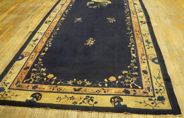 A long navy rug featuring gold and peach floral borders lies on a polished light wood floor.