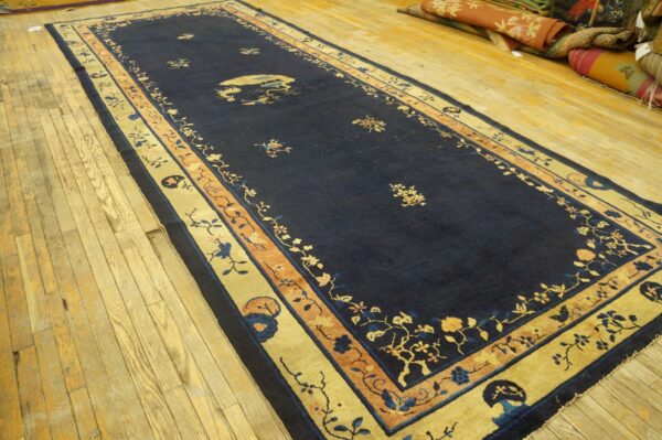 Dark blue runner rug with gold and orange floral borders displayed on wide plank hardwood flooring.