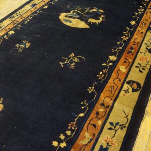 Navy rug with gold and orange floral borders and a central scenic motif lies on light yellow wood flooring.