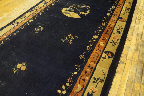 Navy rug with gold and orange floral borders and a central scenic motif lies on light yellow wood flooring.