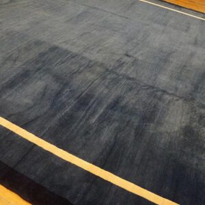 Dark blue area rug with visible sheen and thin yellow stripes resting on a light brown wood floor.