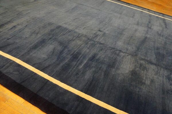Dark blue area rug with visible sheen and thin yellow stripes resting on a light brown wood floor.