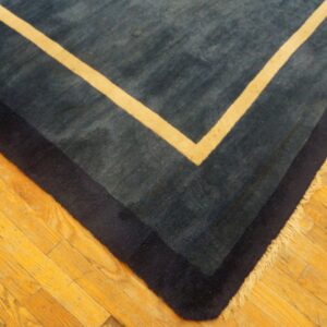Corner of a medium-pile blue rug featuring navy and cream concentric borders on bright hardwood flooring.