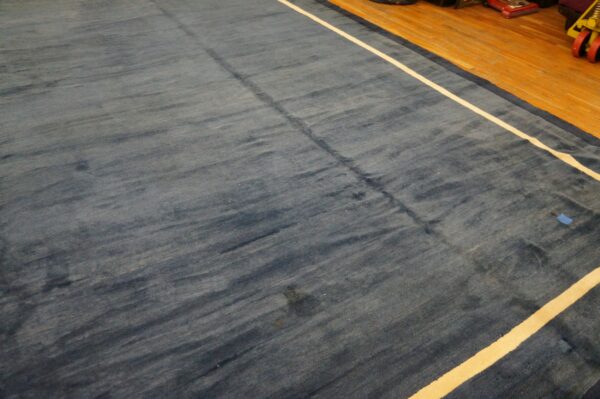 Plush blue rug with abrash texture and a white stripe displayed on light brown hardwood flooring.
