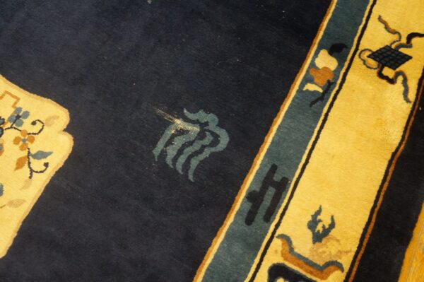 Navy blue rug field contrasts with a yellow border featuring floral patterns and teal and rust accents.