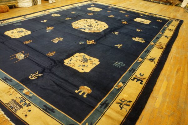Large indigo rug with stylized medallions and symbols has a wide gold border on wood flooring.