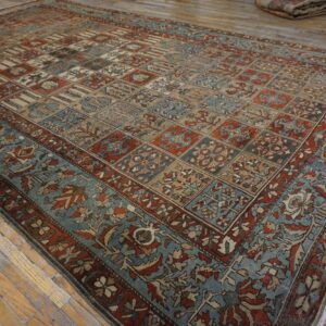Rust and teal rug featuring a paneled motif pattern rests on distressed light wood flooring.