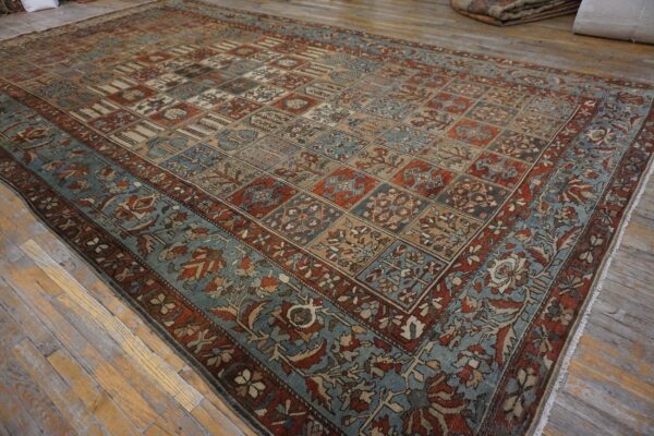 Rust and teal rug featuring a paneled motif pattern rests on distressed light wood flooring.