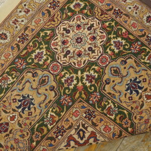 Detailed rug corner with gold, green, and red elaborate patterns rolled over distressed wood flooring.