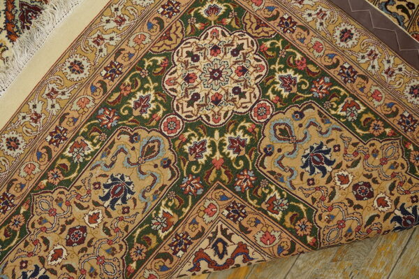 Detailed rug corner with gold, green, and red elaborate patterns rolled over distressed wood flooring.