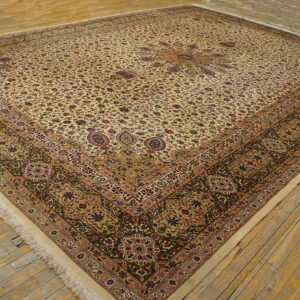 A large square rug with a cream floral pattern and dark green and gold detailed borders on wood flooring.