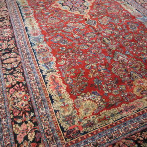 Traditional deep red floral rug with intricate navy and cream borders resting on light wood flooring.