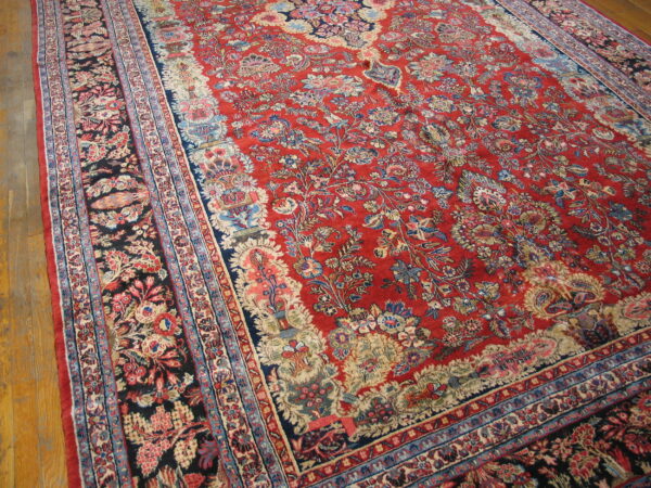 Traditional deep red floral rug with intricate navy and cream borders resting on light wood flooring.