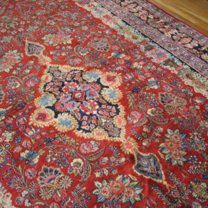 Ornate red rug with a dense multicolored floral pattern and dark blue central motif rests on wood planks.