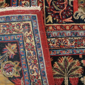 A detailed view of a navy, red, and beige floral patterned rug folded over hardwood flooring.