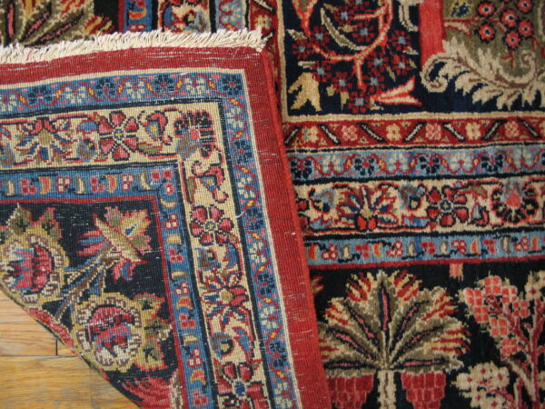 A detailed view of a navy, red, and beige floral patterned rug folded over hardwood flooring.