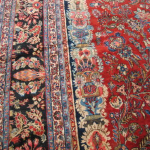 Detailed floral rug featuring a red field, black panel, blue borders, and cream accents on hardwood flooring.