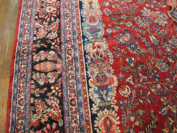 Detailed floral rug featuring a red field, black panel, blue borders, and cream accents on hardwood flooring.