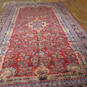 Traditional red rug with blue and cream floral patterns and a central medallion lies on polished wood flooring.