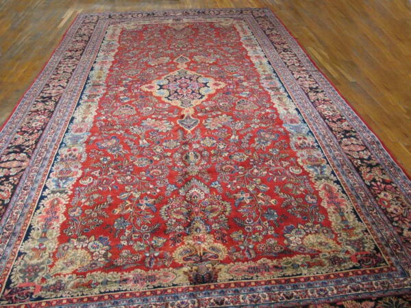 Traditional red rug with blue and cream floral patterns and a central medallion lies on polished wood flooring.