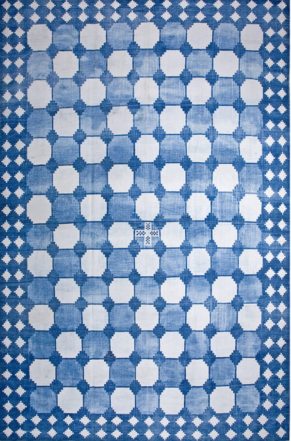 A low-pile blue and white rug displays a faded geometric grid pattern with large white shapes.