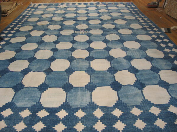 Large blue and white checkerboard rug with a geometric diamond lattice pattern laid on a wood floor.