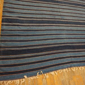 Low-profile blue and navy striped rug with peach accents and fringed ends rests on golden wood flooring.
